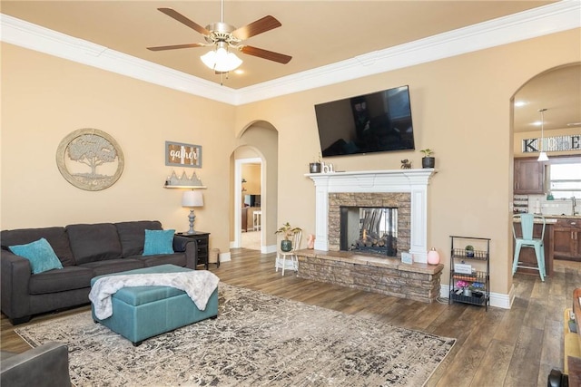 living room featuring ornamental molding, a stone fireplace, ceiling fan, and dark hardwood / wood-style flooring