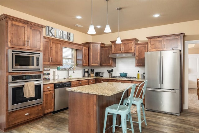 kitchen featuring a breakfast bar, hanging light fixtures, stainless steel appliances, a center island, and light stone countertops