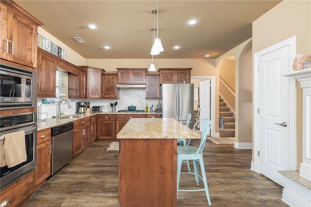 kitchen featuring appliances with stainless steel finishes, hanging light fixtures, a center island, light stone countertops, and a kitchen bar