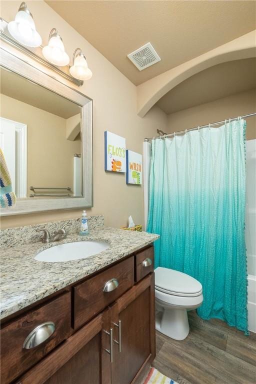 full bathroom with hardwood / wood-style flooring, vanity, shower / tub combo, and toilet