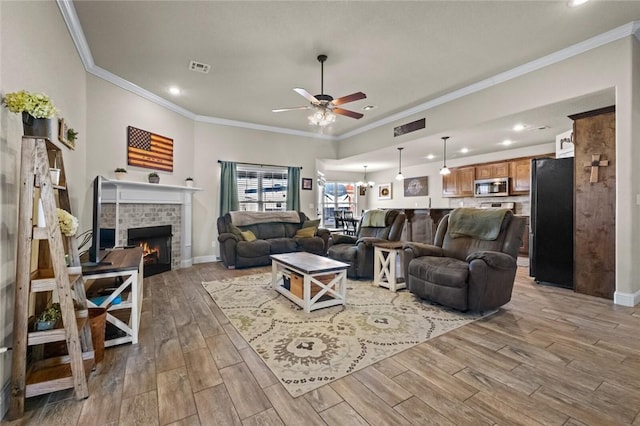 living room featuring ornamental molding, ceiling fan with notable chandelier, a fireplace, and light hardwood / wood-style flooring