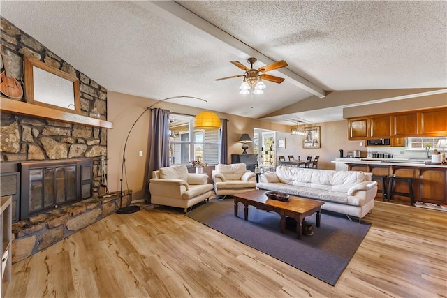 living room featuring ceiling fan, lofted ceiling with beams, a textured ceiling, a stone fireplace, and light wood-type flooring