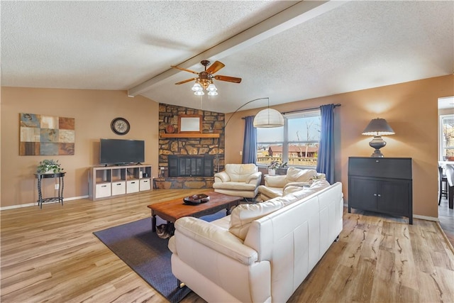 living room with a stone fireplace, vaulted ceiling with beams, a textured ceiling, light wood-type flooring, and ceiling fan