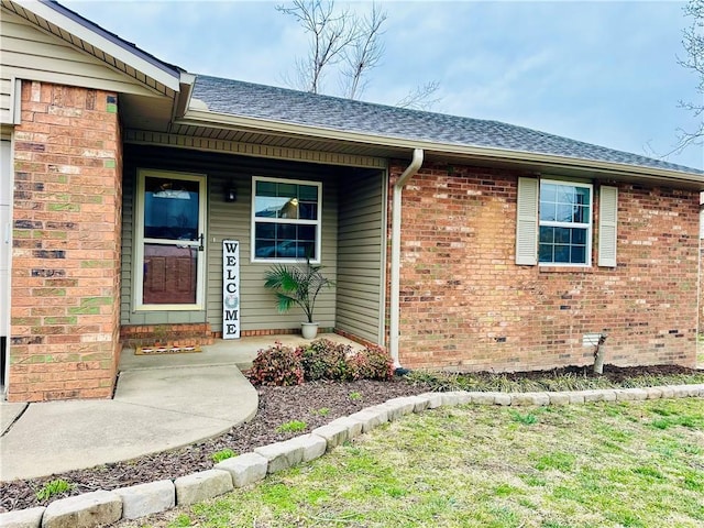 view of exterior entry with roof with shingles and brick siding