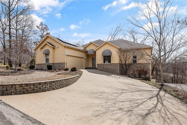 single story home with concrete driveway, brick siding, an attached garage, and roof mounted solar panels