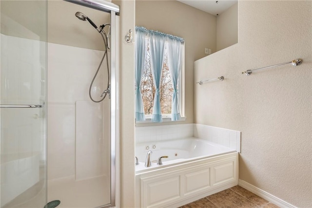 bathroom with a textured wall, a shower stall, a bath, and baseboards