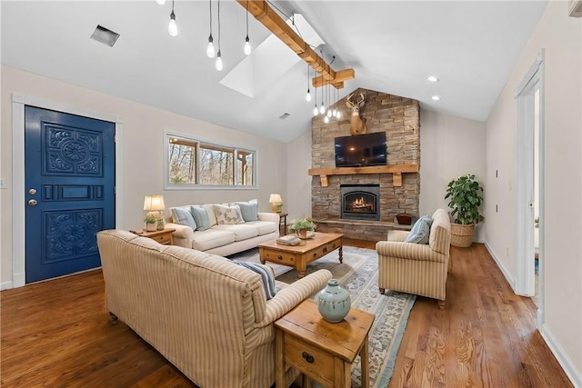 living area featuring vaulted ceiling with skylight, a fireplace, baseboards, and wood finished floors