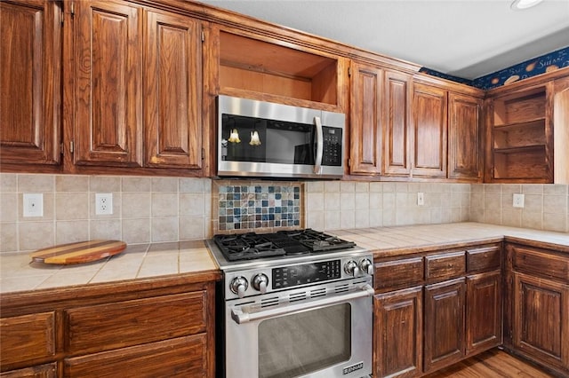 kitchen with tasteful backsplash, tile counters, light wood-style flooring, stainless steel appliances, and open shelves