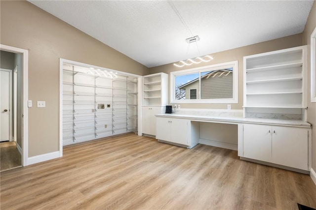 unfurnished office with built in desk, light hardwood / wood-style floors, a textured ceiling, and vaulted ceiling