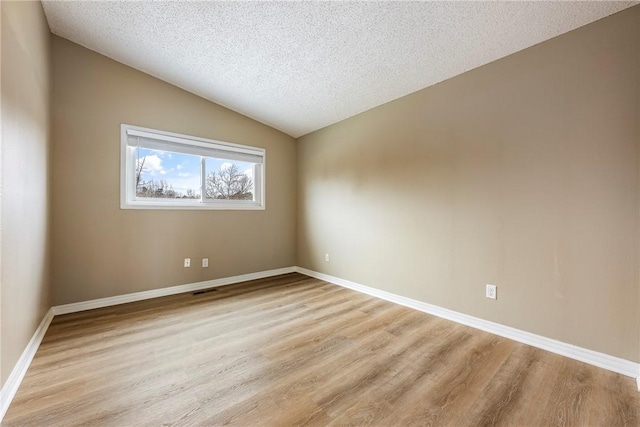 empty room with vaulted ceiling, light hardwood / wood-style flooring, and a textured ceiling