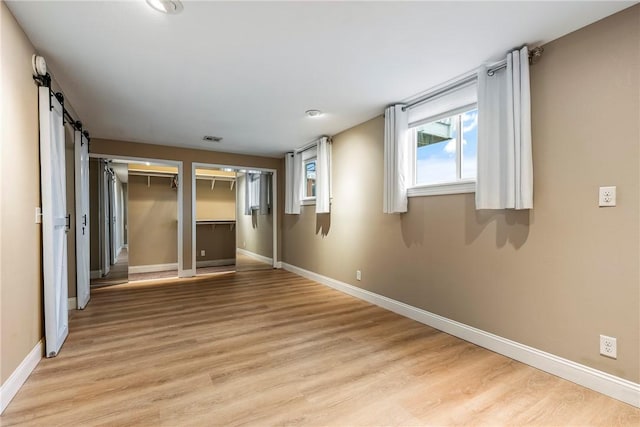 unfurnished bedroom with two closets, a barn door, and light wood-type flooring