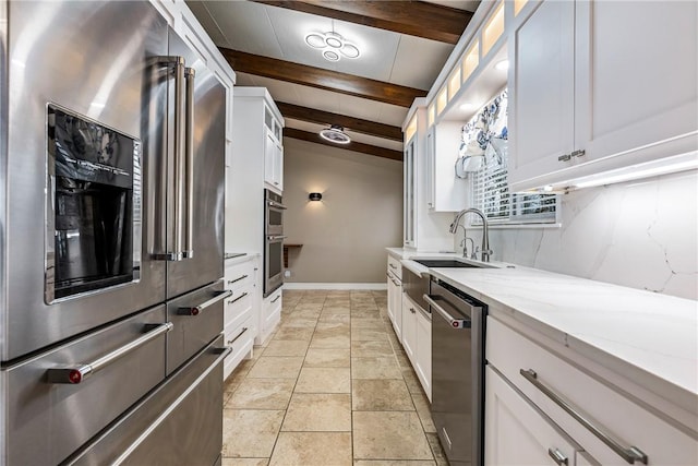 kitchen with white cabinetry, sink, light stone counters, stainless steel appliances, and beam ceiling