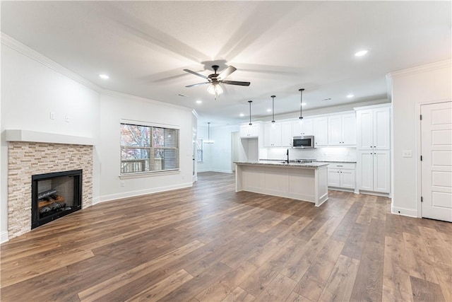 kitchen featuring white cabinetry, hardwood / wood-style floors, light stone counters, a center island with sink, and decorative light fixtures