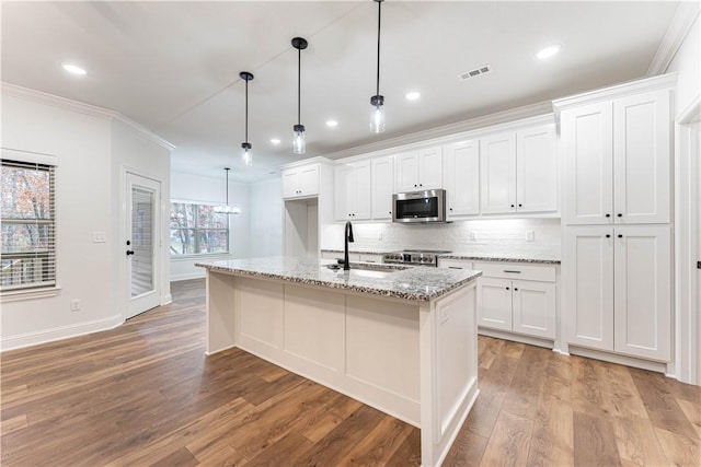 kitchen with pendant lighting, sink, white cabinets, light stone counters, and a center island with sink