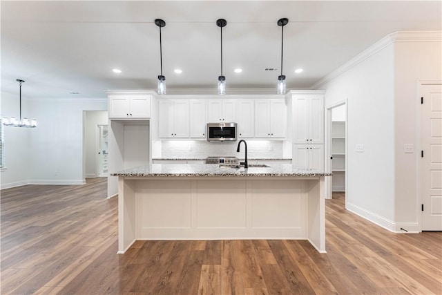 kitchen featuring pendant lighting, sink, white cabinetry, light stone countertops, and an island with sink