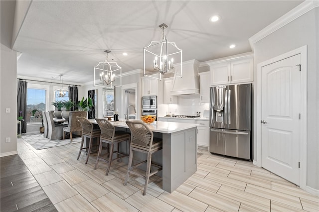 kitchen with appliances with stainless steel finishes, decorative light fixtures, an island with sink, white cabinets, and an inviting chandelier