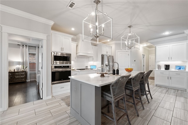 kitchen with white cabinetry, an inviting chandelier, decorative light fixtures, appliances with stainless steel finishes, and a kitchen island with sink