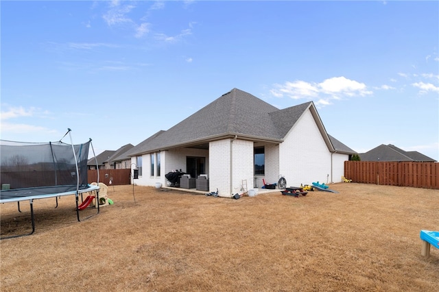 rear view of property featuring a trampoline and a lawn