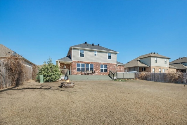 rear view of house with a wooden deck, a lawn, and a fire pit