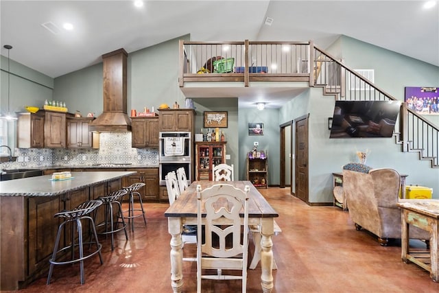 kitchen with premium range hood, high vaulted ceiling, a sink, backsplash, and finished concrete floors