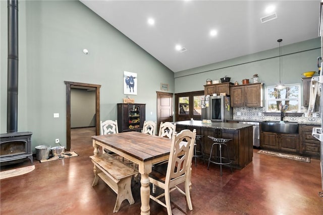 dining room with a wood stove, high vaulted ceiling, visible vents, and finished concrete floors