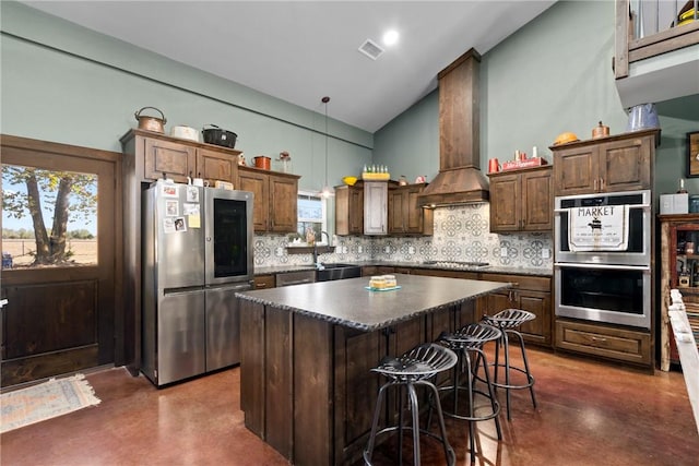 kitchen featuring stainless steel appliances, custom exhaust hood, decorative backsplash, dark countertops, and finished concrete floors