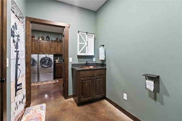 clothes washing area featuring washer and clothes dryer, a sink, a barn door, cabinet space, and baseboards