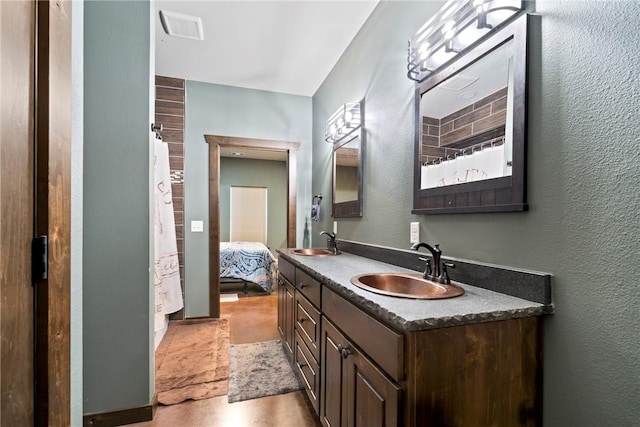 full bath with a textured wall, visible vents, and a sink