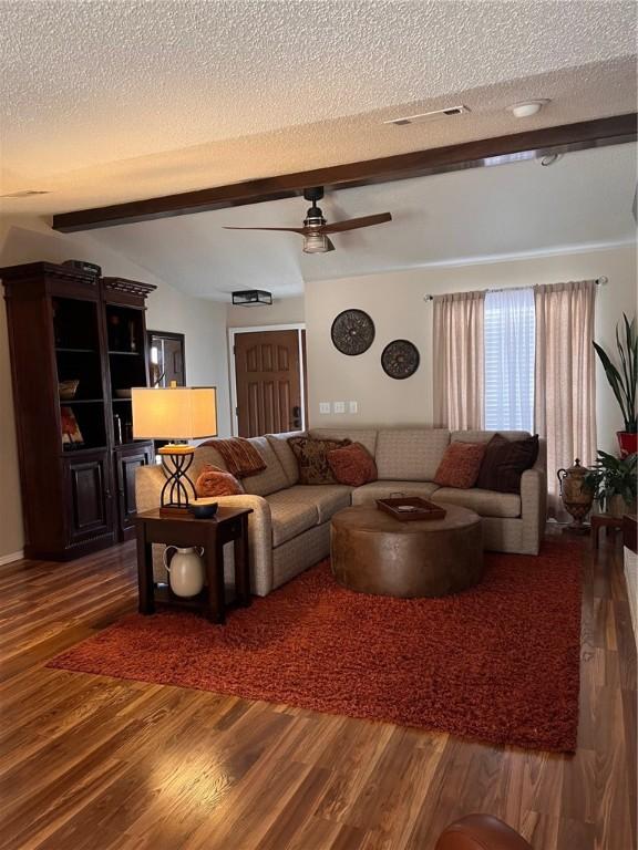 living area featuring a textured ceiling, beamed ceiling, wood finished floors, and ceiling fan