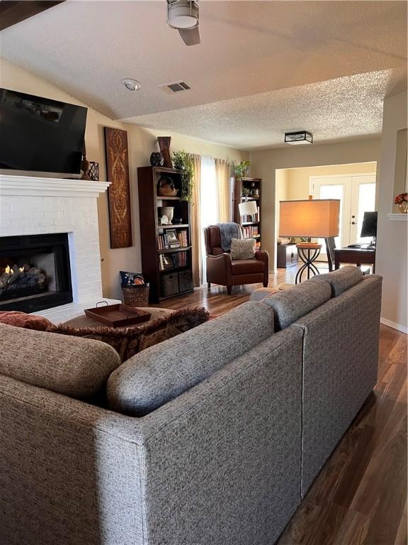 living room featuring visible vents, dark wood finished floors, lofted ceiling, a textured ceiling, and a brick fireplace