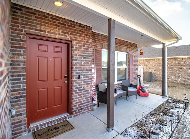 snow covered property entrance with central AC and a porch