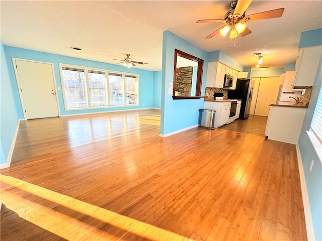 unfurnished living room with ceiling fan, sink, and light hardwood / wood-style flooring