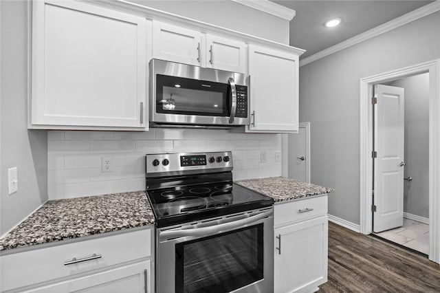 kitchen with white cabinets, dark stone counters, ornamental molding, stainless steel appliances, and dark wood-type flooring