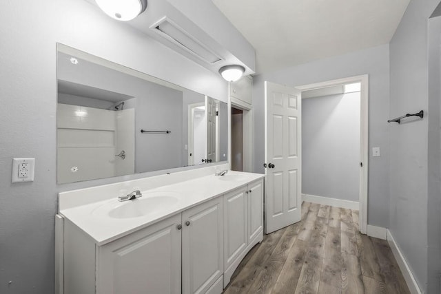 full bathroom featuring wood finished floors, double vanity, and baseboards