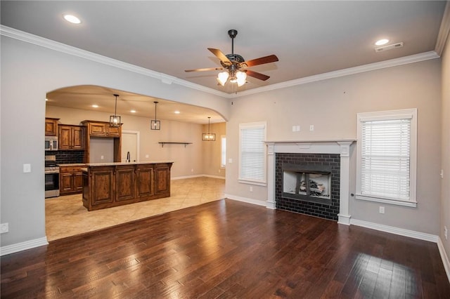 living room featuring a tile fireplace, ornamental molding, ceiling fan, and light wood-type flooring