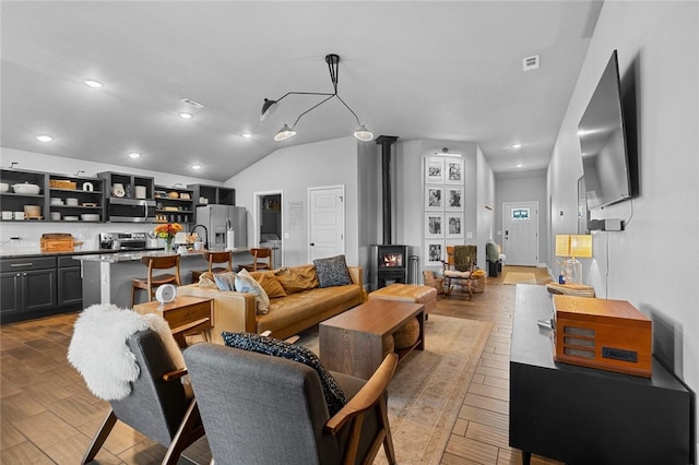 living room with wood-type flooring, vaulted ceiling, and a wood stove