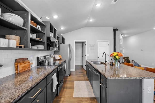 kitchen with lofted ceiling, sink, appliances with stainless steel finishes, a kitchen island with sink, and hardwood / wood-style floors