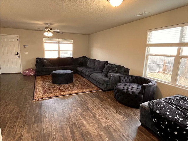 living room featuring dark wood-type flooring, ceiling fan, and a textured ceiling