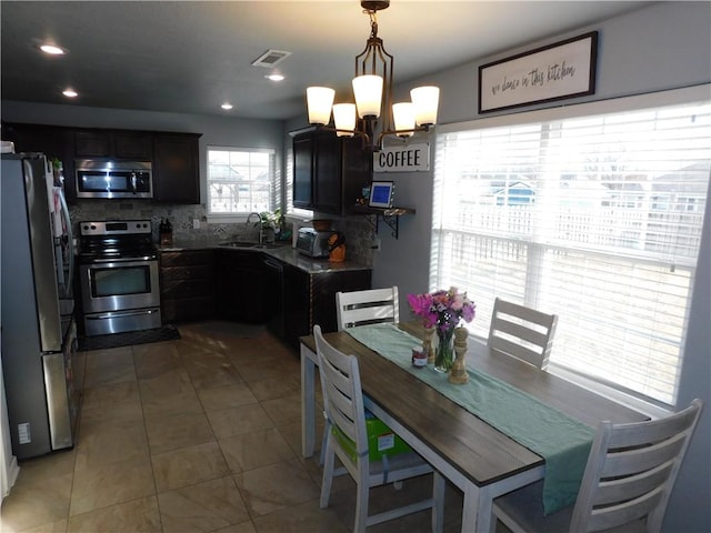 kitchen with sink, dark tile patterned flooring, stainless steel appliances, hanging light fixtures, and tasteful backsplash