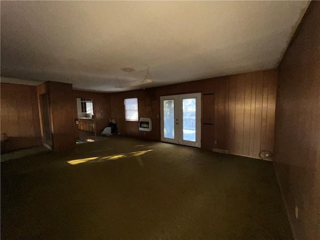 unfurnished living room featuring heating unit, french doors, carpet flooring, and wood walls