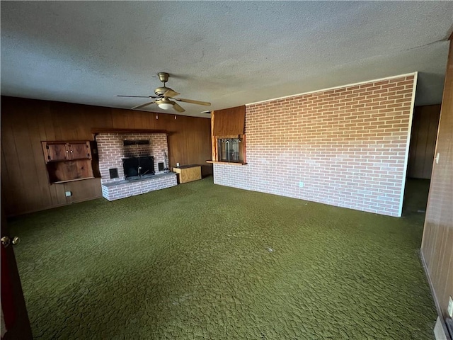 unfurnished living room featuring a fireplace, wood walls, dark carpet, ceiling fan, and a textured ceiling