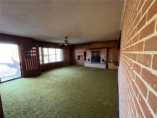 unfurnished living room featuring ceiling fan, wooden walls, carpet floors, and a textured ceiling