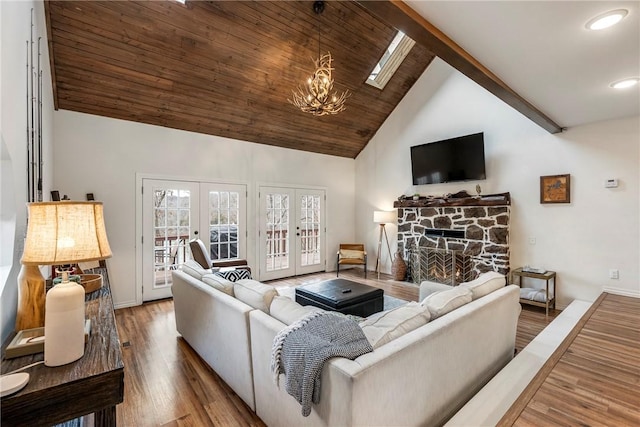 living room featuring french doors, an inviting chandelier, a stone fireplace, wood finished floors, and high vaulted ceiling