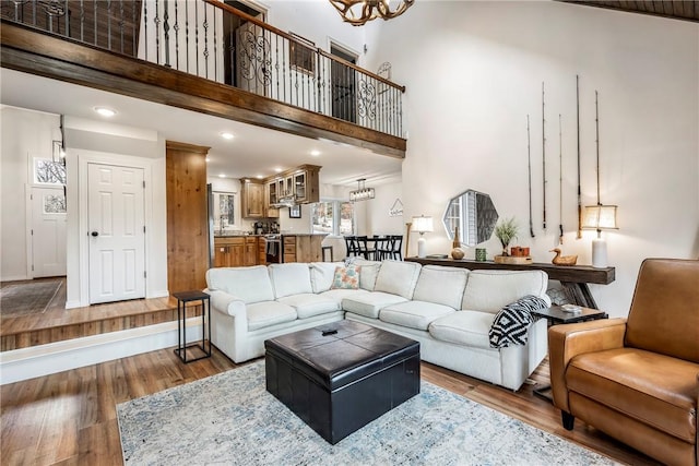 living room featuring recessed lighting, a notable chandelier, wood finished floors, a towering ceiling, and baseboards