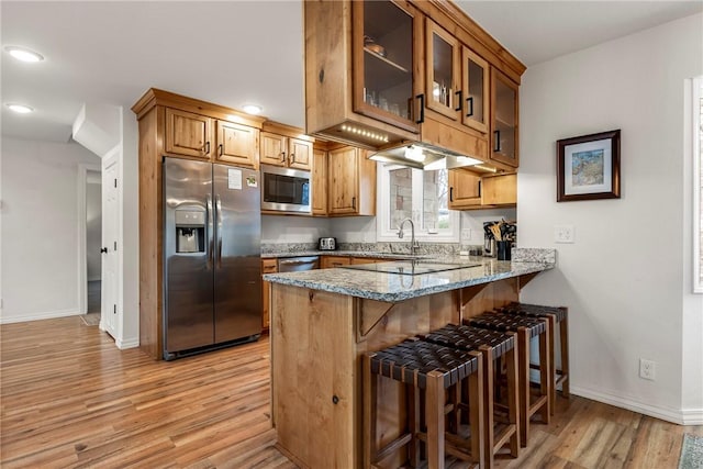 kitchen featuring a breakfast bar area, appliances with stainless steel finishes, stone countertops, glass insert cabinets, and a peninsula