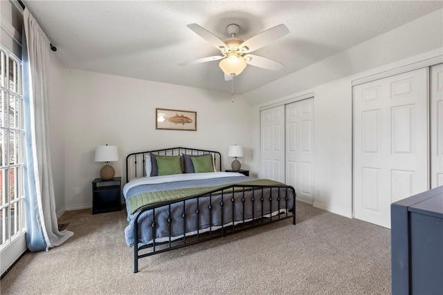 carpeted bedroom with a textured ceiling, ceiling fan, multiple windows, and two closets