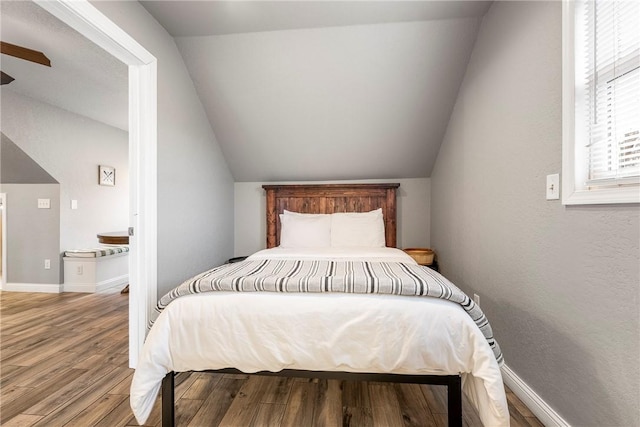 bedroom featuring lofted ceiling, baseboards, and wood finished floors