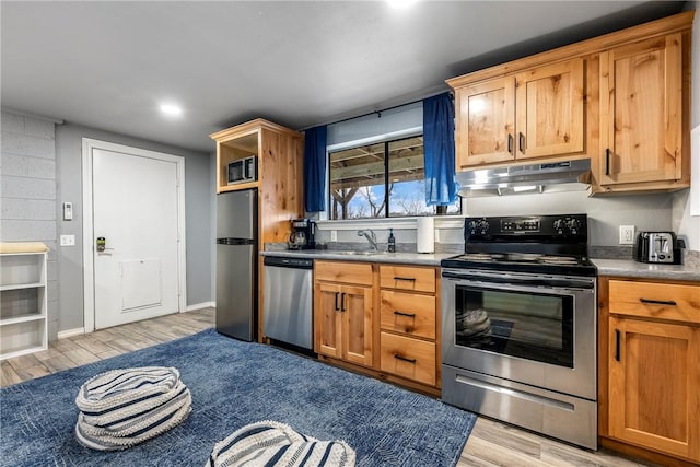 kitchen with under cabinet range hood, a sink, light wood-style floors, appliances with stainless steel finishes, and dark countertops