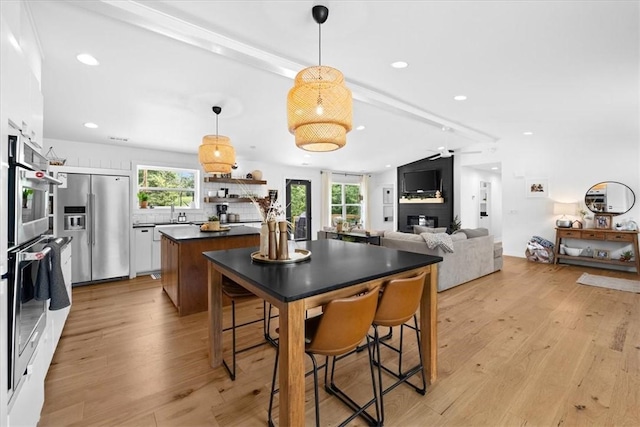 kitchen featuring high end refrigerator, open floor plan, open shelves, light wood finished floors, and dark countertops