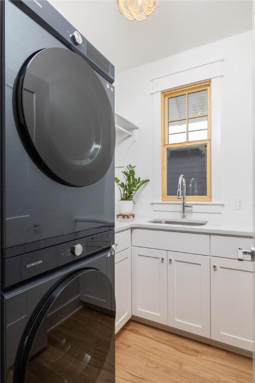 washroom with light wood-type flooring, stacked washer and dryer, a sink, and cabinet space